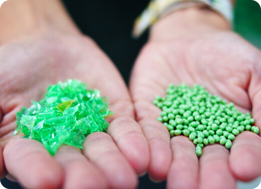 Two hands holding green pellets of recycled plastic